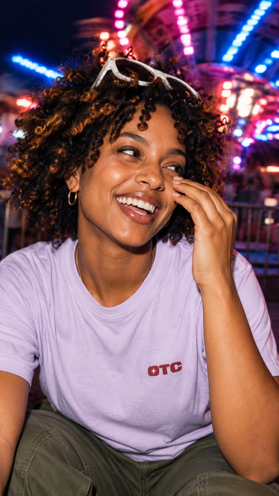 A model laughing at a fairground at night in the Same Show Tee in lavender, front view