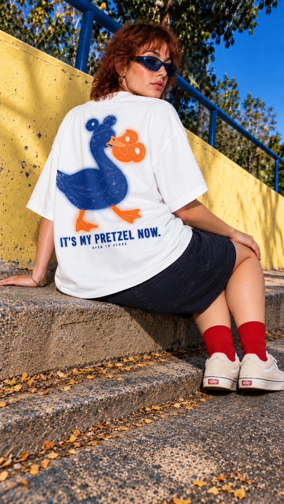 It’s My Pretzel Now Oversized Tee worn by a model, back view, on concrete steps