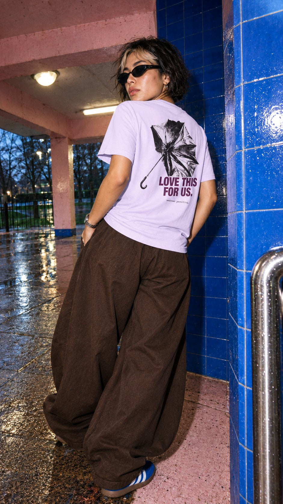 Love This for Us Tee worn by a model, back view, by a tiled pillar in the rain