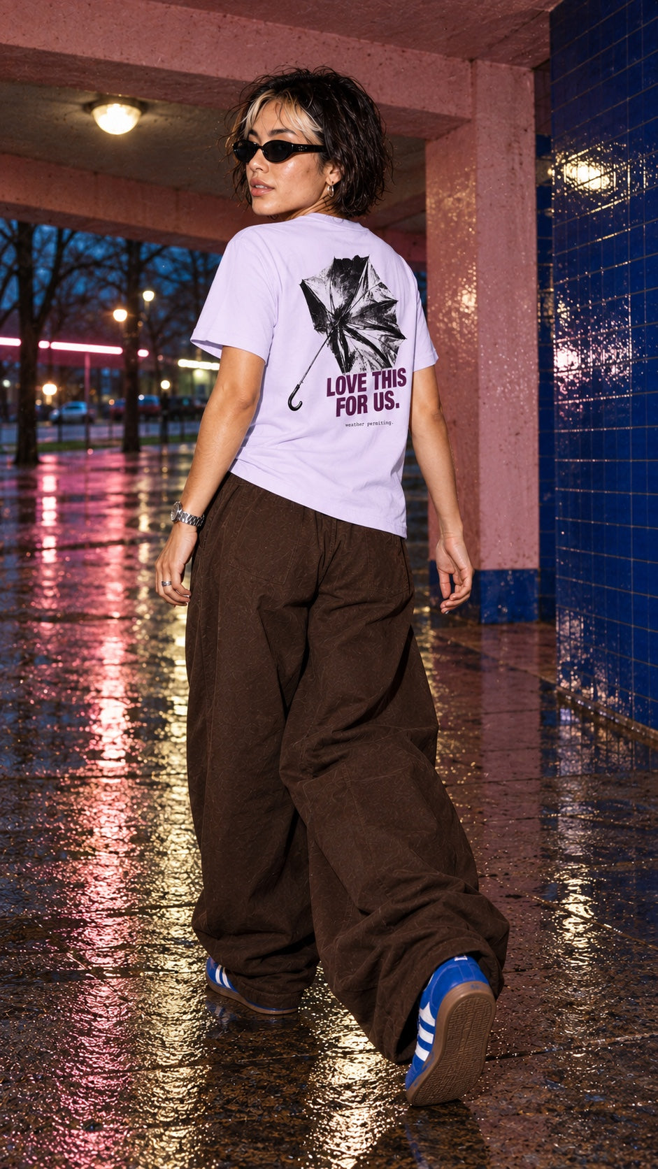 Love This for Us Tee in lavender worn by a model, back view, walking by a tiled pillar in the rain