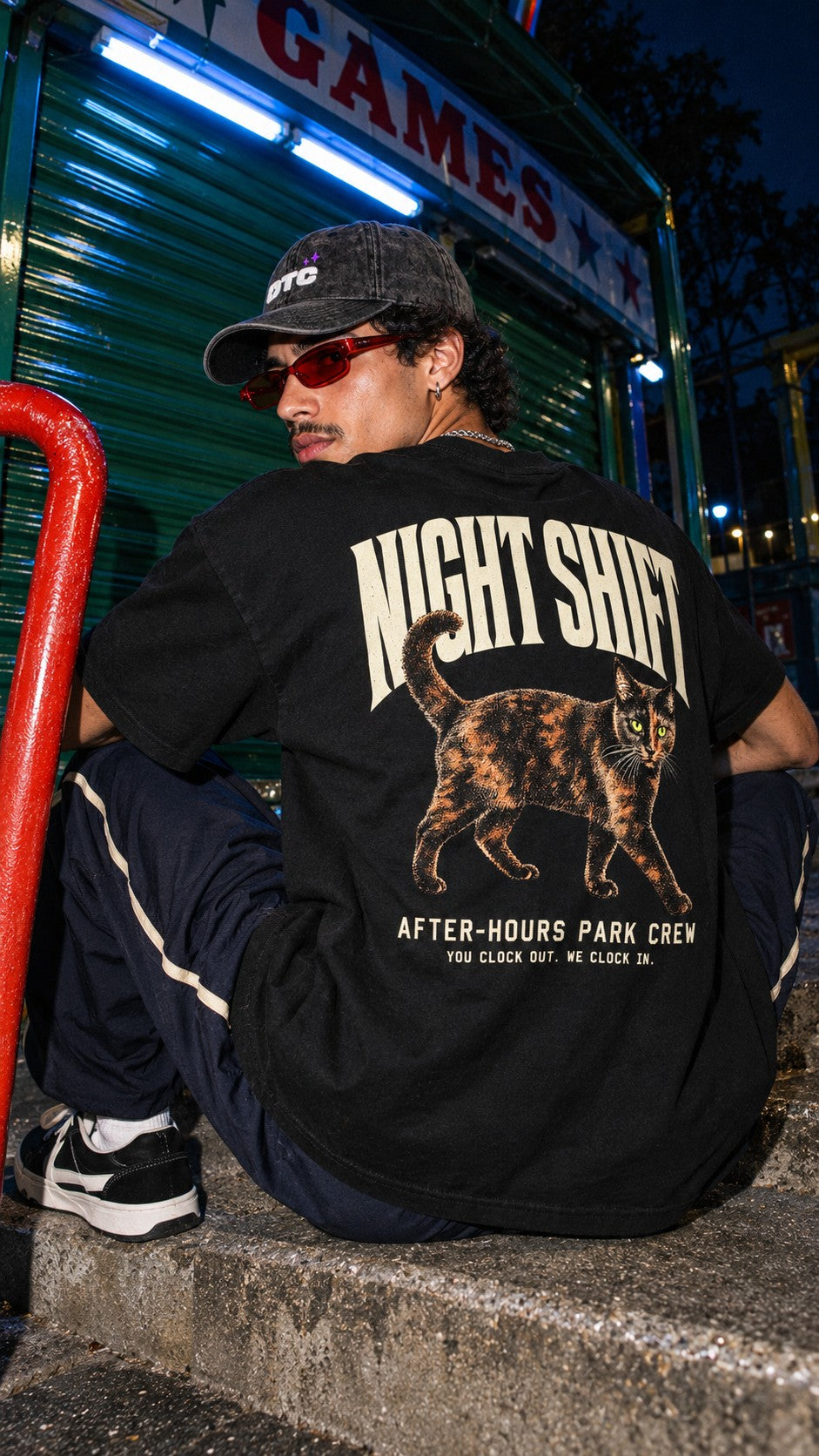 Night Shift Boxy Tee worn by a model, back view, outside the games arcade at night