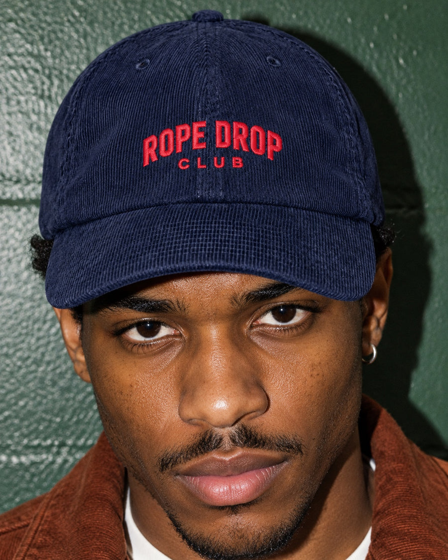 Rope Drop Club Corduroy Cap in navy worn by a model, front view, with red Rope Drop Club embroidery