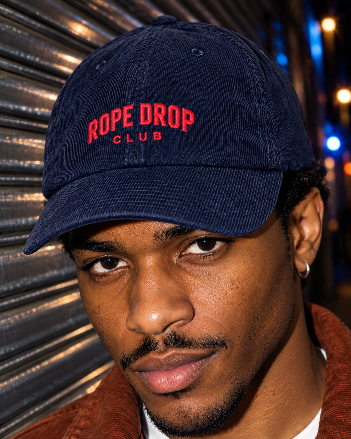 Rope Drop Club Corduroy Cap in navy worn by a model on a street at night, front view