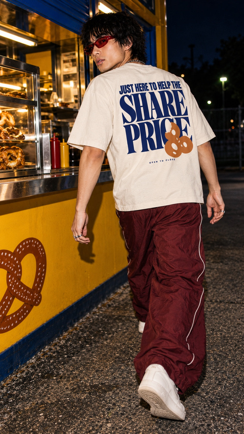 Share Price Boxy Tee worn by a model, back view, walking past a pretzel stand at night