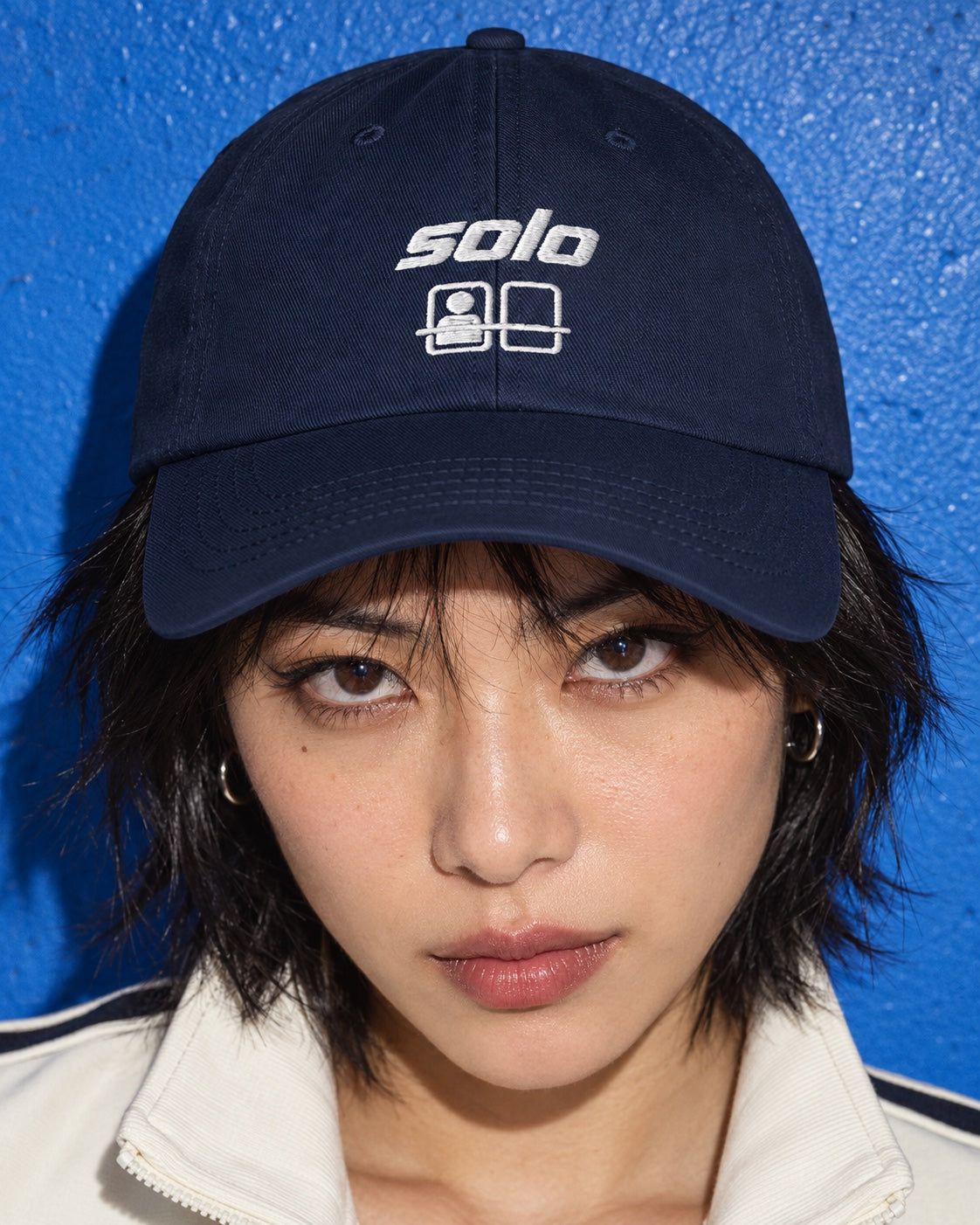 Solo Cap in navy worn by a model, front view, with white “solo” embroidery and a ride-seat motif